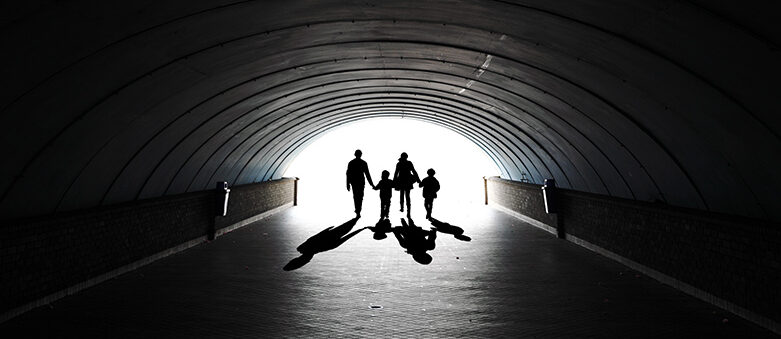 Silhouetted family, reminiscent of musings on the new lockdown back in April last year, holds hands while walking through a tunnel towards bright light. Shadows stretch on the tunnel floor.