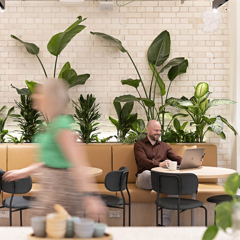 A man works on a laptop while somebody walks past