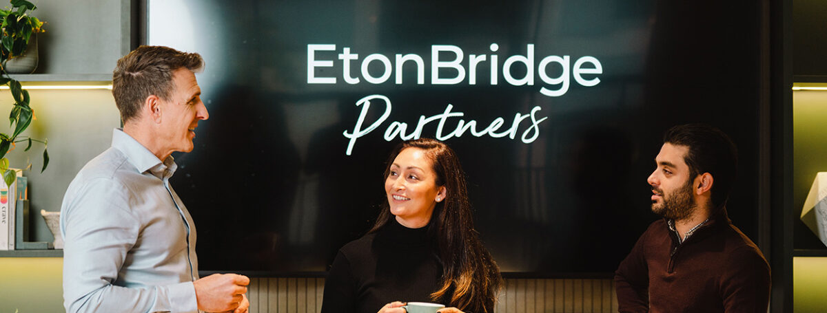Eton Bridge Partners meeting room, with logo on the TV and a group of people talking