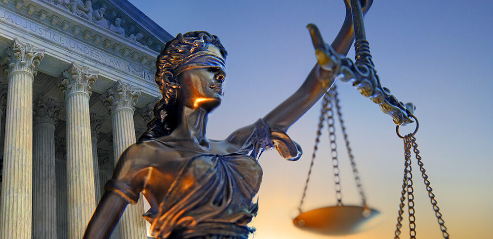 A statue of the blindfolded lady justice in front of the United States Supreme Court building as the sun rises in the distance symbolizing the dawning of a new era.